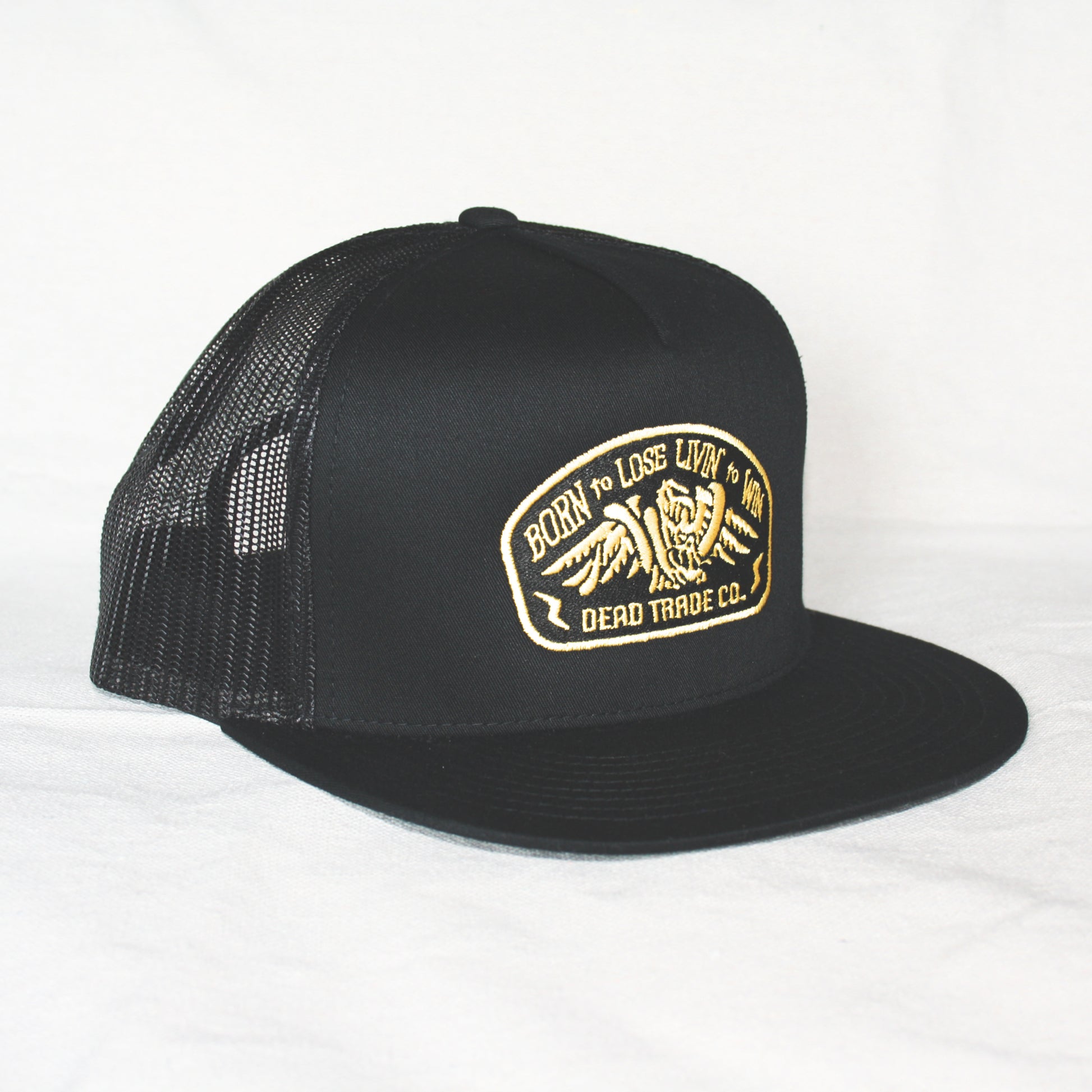 Black snapback with 'Born to Lose' gold embroidery on the front panel. High-profile, flat-brim trucker cap with breathable mesh. Made of 65% polyester, 35% cotton. Structured 5-panel, 4” crown. Finished in Alberta, Canada.