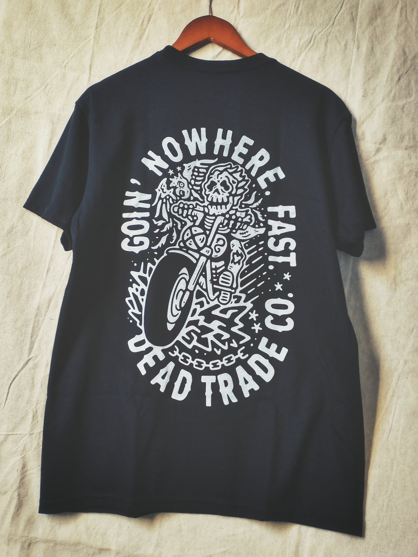 Black graphic t-shirt made in Canada from a soft 50/50 poly-cotton blend, featuring a bold hand-drawn design of a biker skeleton riding a motorcycle, screen printed in white ink. Perfect for those who appreciate lowbrow, edgy artwork.