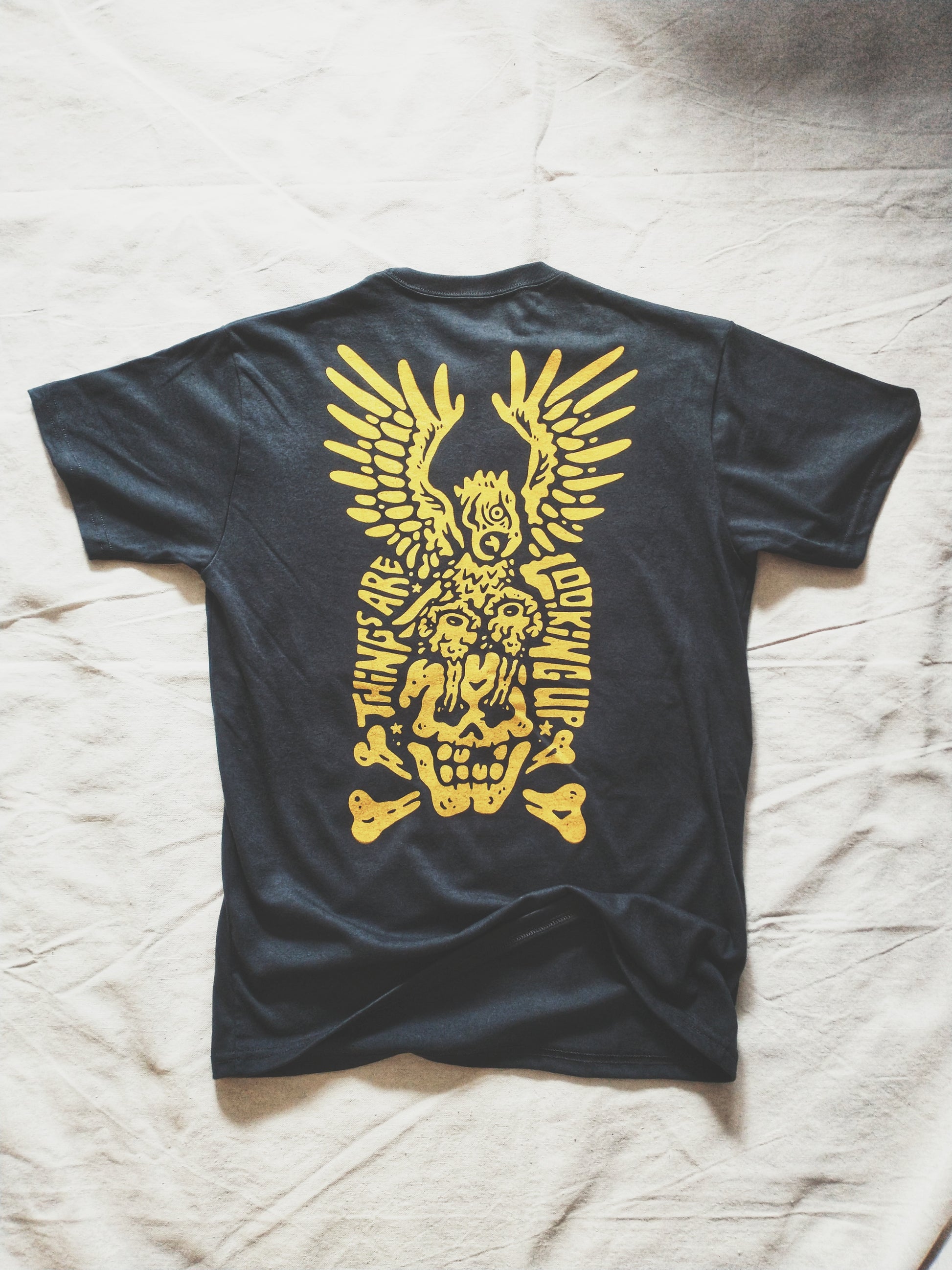 Charcoal graphic t-shirt made in Canada from a soft 50/50 poly-cotton blend, featuring a bold hand-drawn design of an eagle pulling eyeballs from a skull, screen printed in vibrant yellow ink. Perfect for those who appreciate lowbrow, edgy artwork.