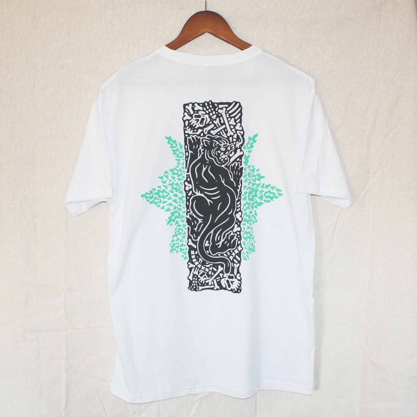 White graphic t-shirt made in Canada from a soft 100% ring-spun cotton, featuring a bold hand-drawn design of a panther on a pit of bones, screen printed in black and light green ink. Perfect for those who appreciate lowbrow, tattoo-style artwork.