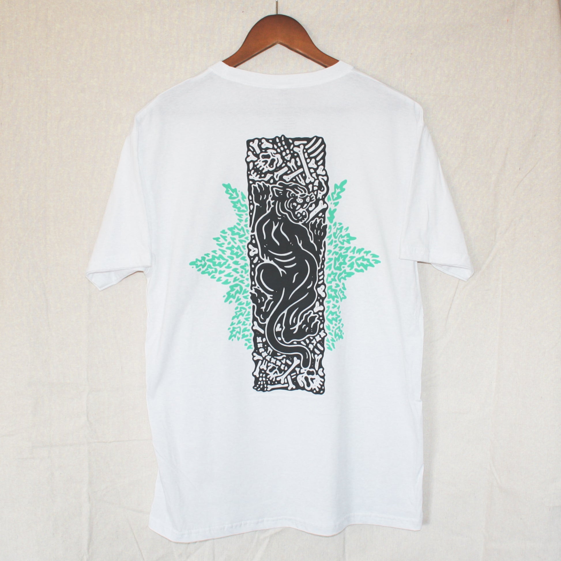 White graphic t-shirt made in Canada from a soft 100% ring-spun cotton, featuring a bold hand-drawn design of a panther on a pit of bones, screen printed in black and light green ink. Perfect for those who appreciate lowbrow, tattoo-style artwork.