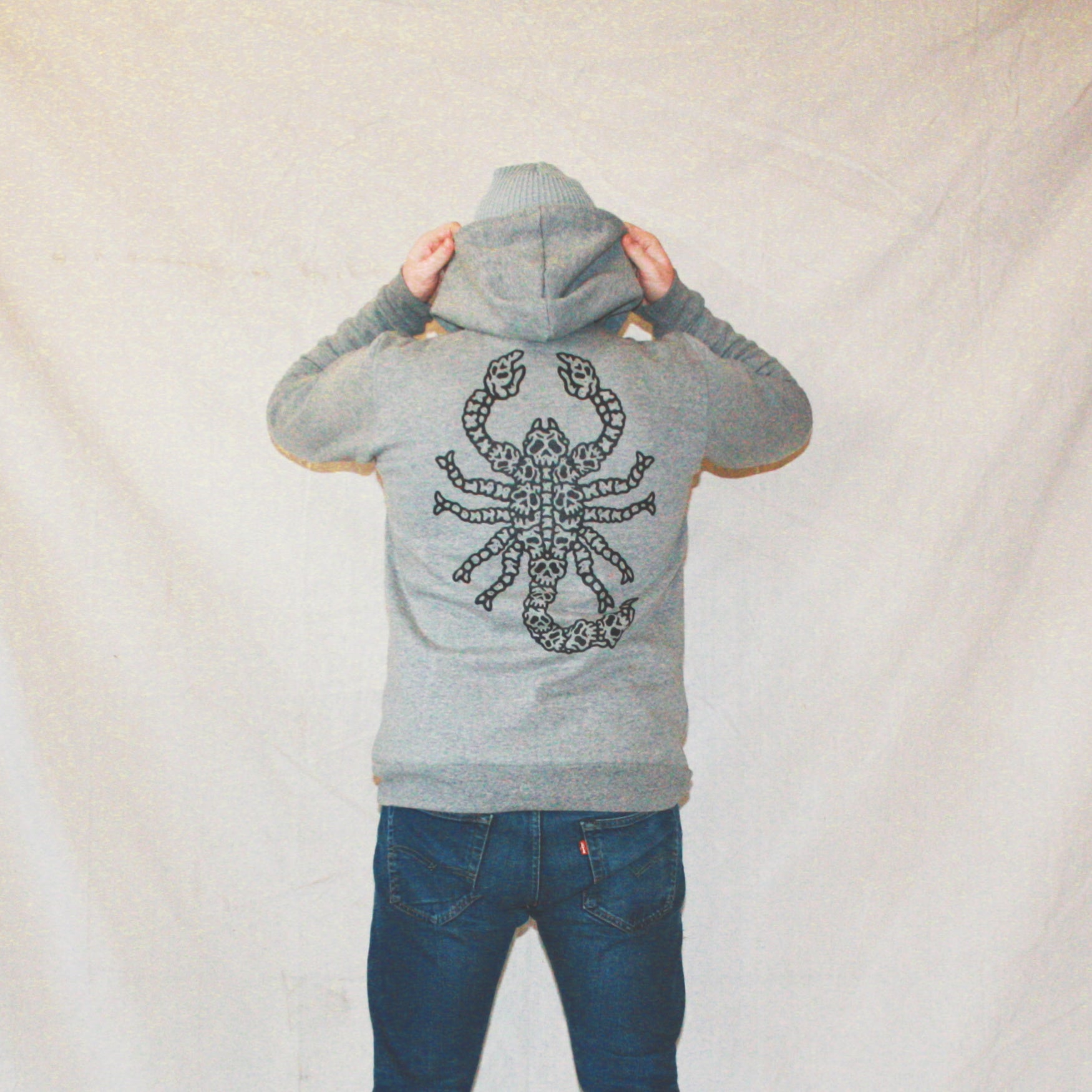 Grey colour, high-quality, made-in-Canada hoodie featuring a hand-drawn scorpion made of skulls screen printed in black on the back. Crafted with 50/50 ring-spun poly/cotton fleece, soft feel, reduced pilling, and durability. Unisex size, 14oz, perfect for cold Canadian winters.