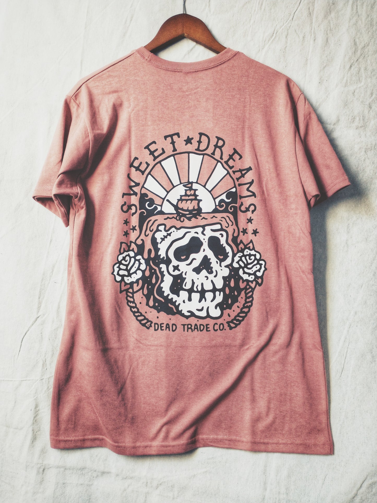 Dusty rose graphic t-shirt made in Canada from a soft 50/50 poly-cotton blend, featuring a bold hand-drawn design of a skull dreaming of sailing the seas, screen printed in black and white ink. Perfect for those who appreciate lowbrow, edgy artwork.