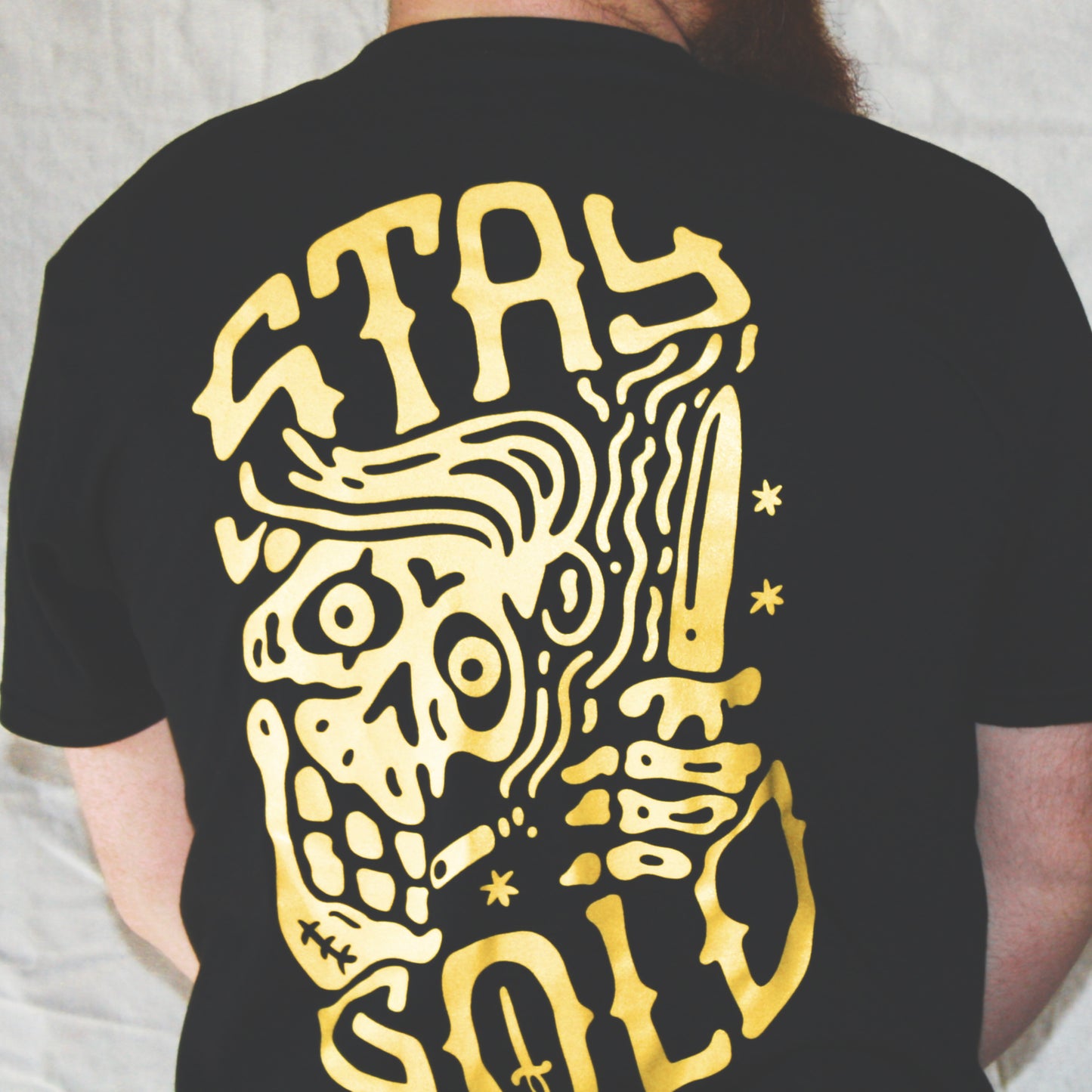 Black graphic t-shirt made in Canada from a soft 100% ring-spun cotton, featuring a bold hand-drawn design of a smiling skeleton holding a switchblade with the words “stay gold,” screen printed in yellow ink. Perfect for those who appreciate lowbrow, edgy artwork.